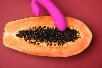 Photo of Half of papaya and purple vibrator on red background, top view. Sex concept