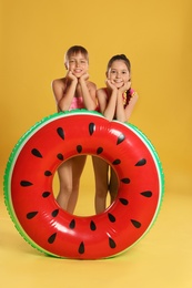 Cute little girls with bright inflatable ring on yellow background