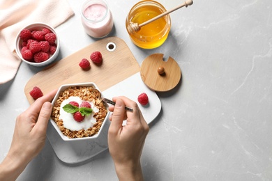 Photo of Woman eating delicious yogurt with granola and raspberries at grey table, top view. Space for text