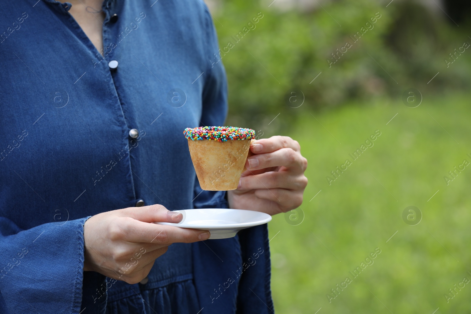 Photo of Woman with delicious edible biscuit cup of coffee decorated with sprinkles outdoors, closeup. Space for text