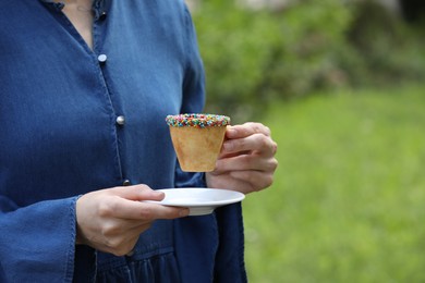 Photo of Woman with delicious edible biscuit cup of coffee decorated with sprinkles outdoors, closeup. Space for text