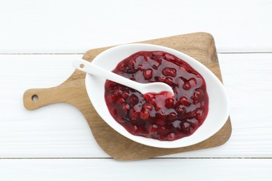 Photo of Fresh cranberry sauce in bowl and spoon on white wooden table, top view