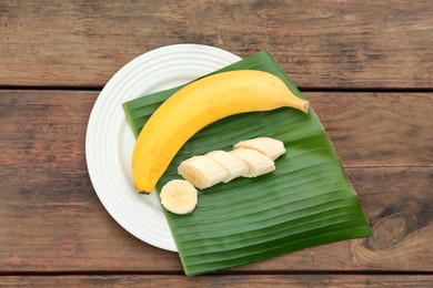 Photo of Plate with delicious bananas and fresh leaf on wooden table, top view