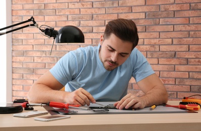 Photo of Technician repairing broken smartphone at table in workshop