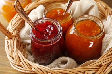 Photo of Jars with different sweet jam in wicker basket, closeup