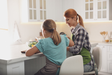 Photo of Mother and daughter cooking salad together in kitchen