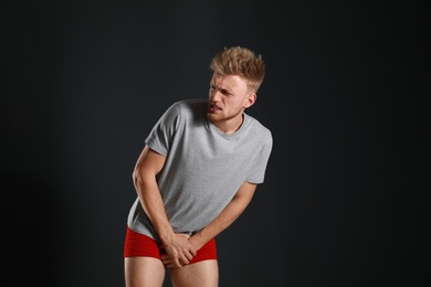 Photo of Young man suffering from pain on black background. Urology problems