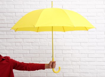 Woman with open yellow umbrella near white brick wall, closeup
