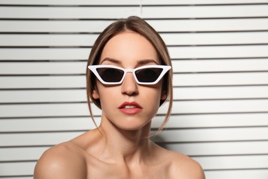 Photo of Young woman wearing stylish sunglasses against blinds