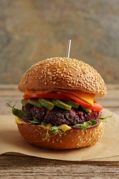 Photo of Tasty vegetarian burger with beet cutlet, cheese, avocado and tomato on wooden table