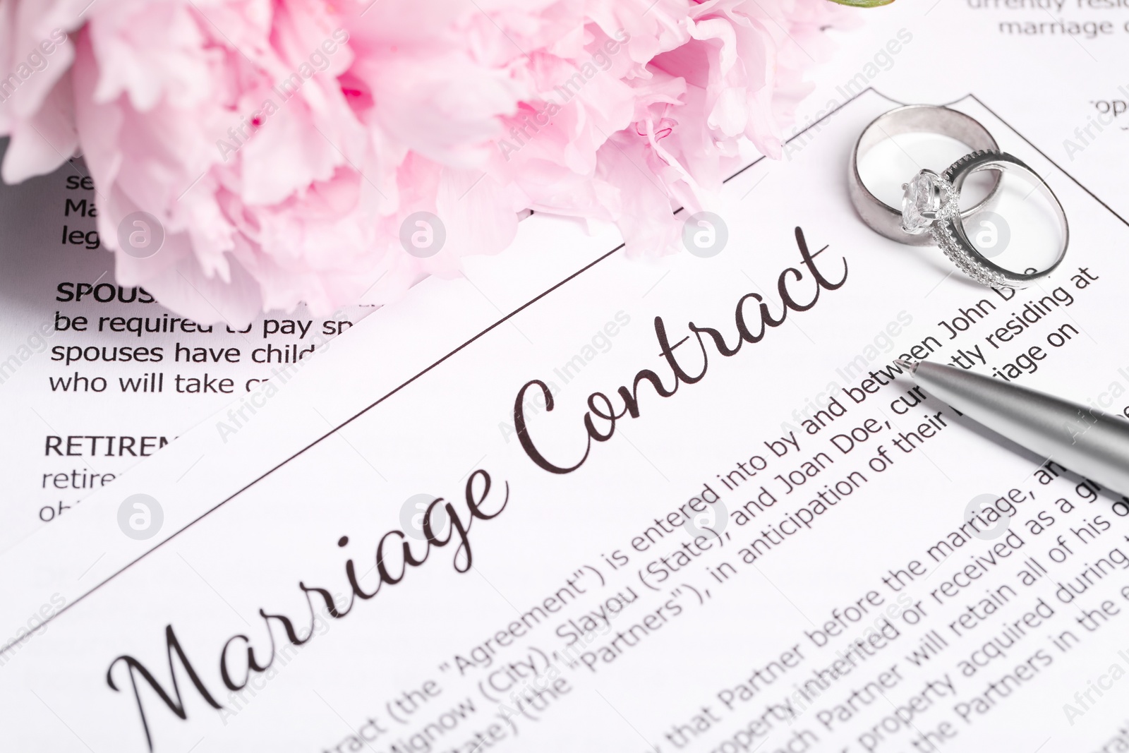 Photo of Marriage contract, wedding rings, pen and flowers on table, closeup