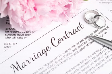 Marriage contract, wedding rings, pen and flowers on table, closeup