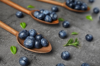 Wooden spoons with tasty blueberries and leaves on grey stone surface