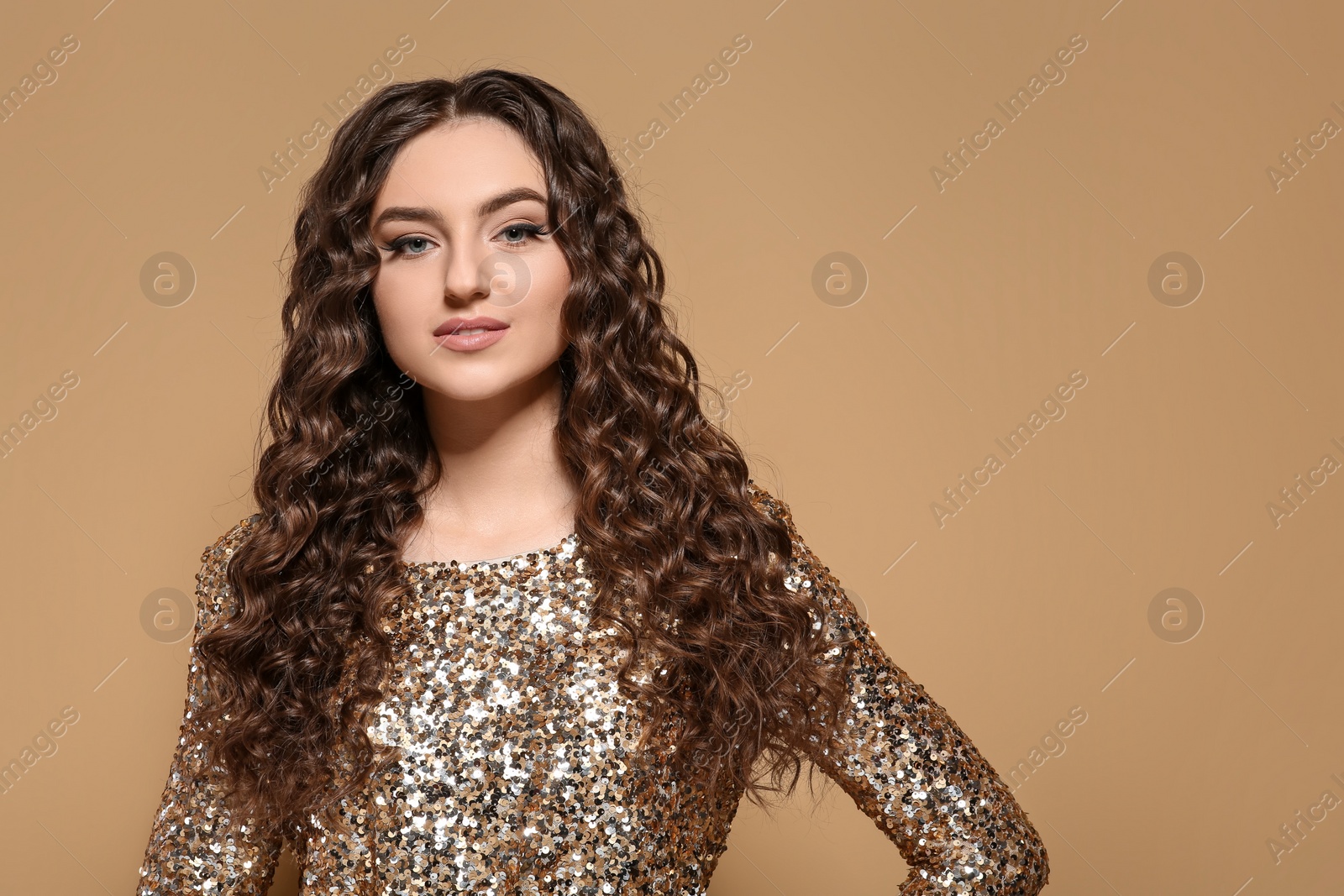 Photo of Beautiful young woman with long curly brown hair in golden sequin dress on beige background