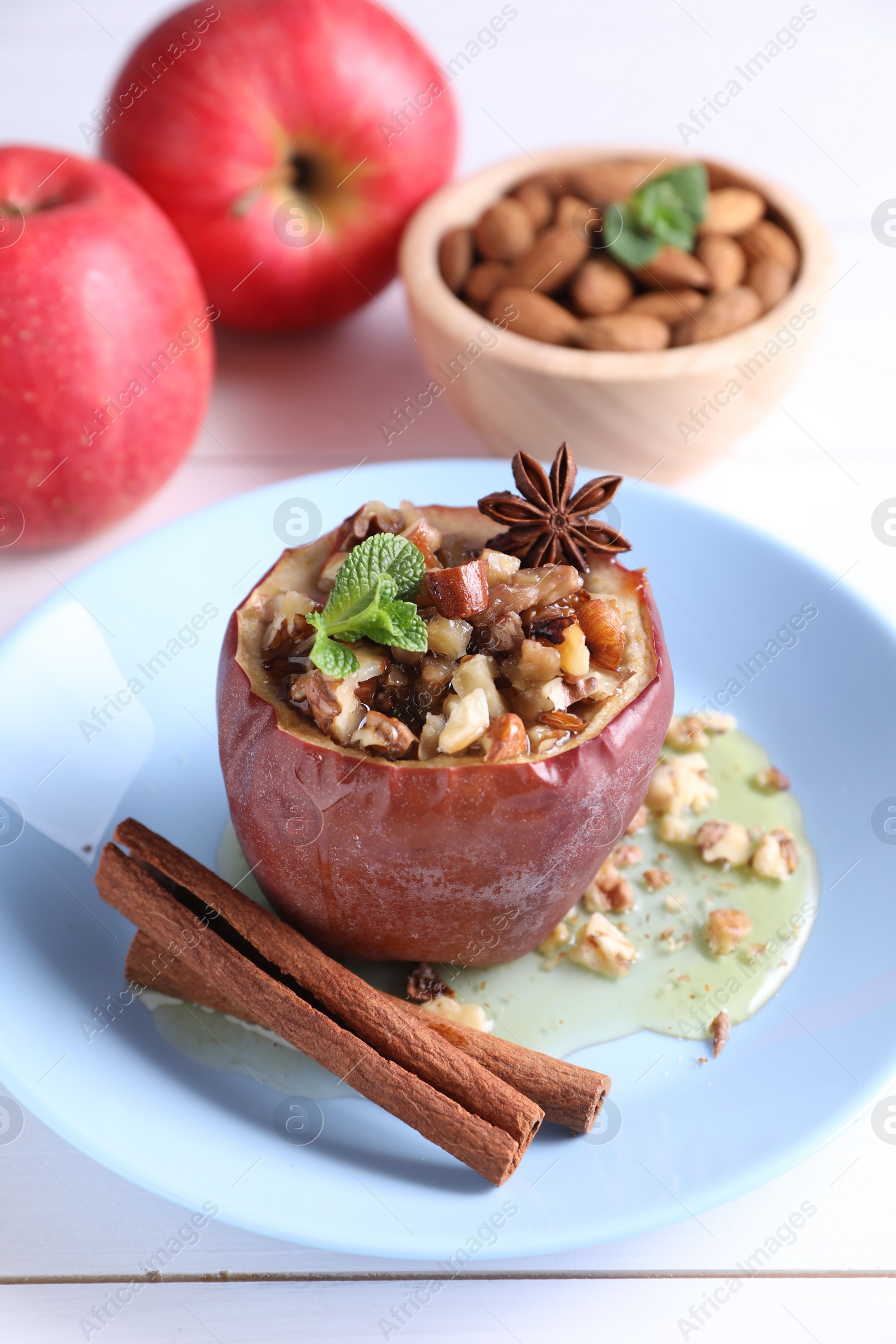 Photo of Tasty baked apple with nuts, honey, spices and mint on white wooden table