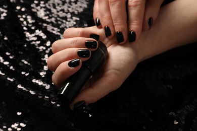 Photo of Woman with black manicure and nail polish bottle on dark background, closeup