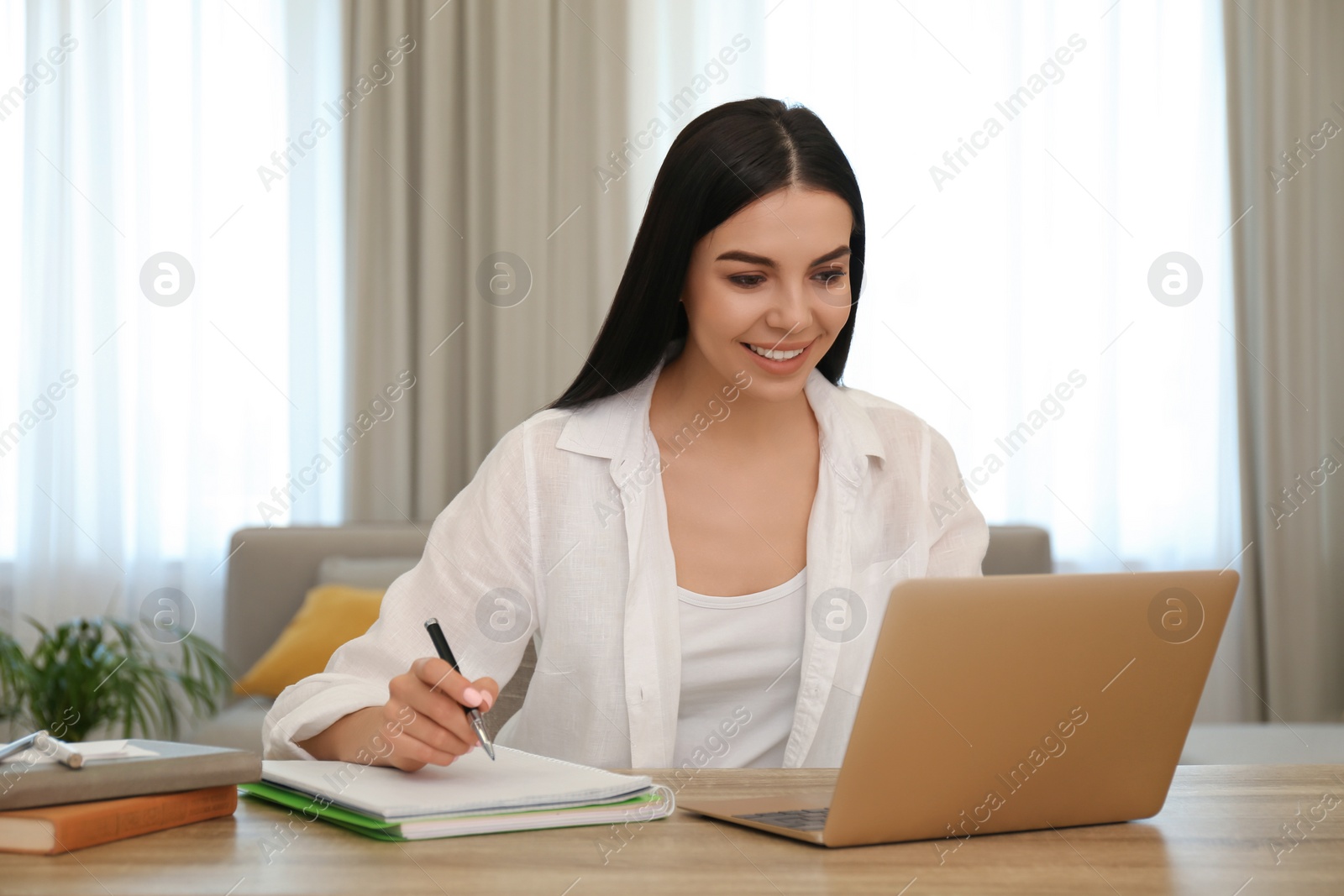 Photo of Young woman taking notes during online webinar at table indoors