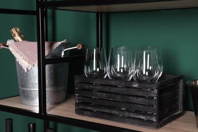 Crate with wine glasses and bucket on rack near green wall