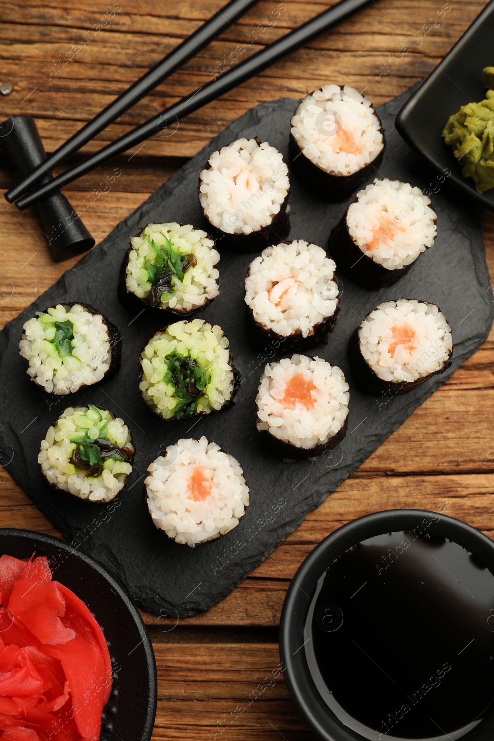 Photo of Tasty sushi rolls served on wooden table, flat lay