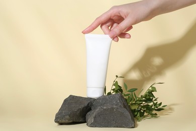 Woman with tube of cream, branches and stones on light yellow background, closeup