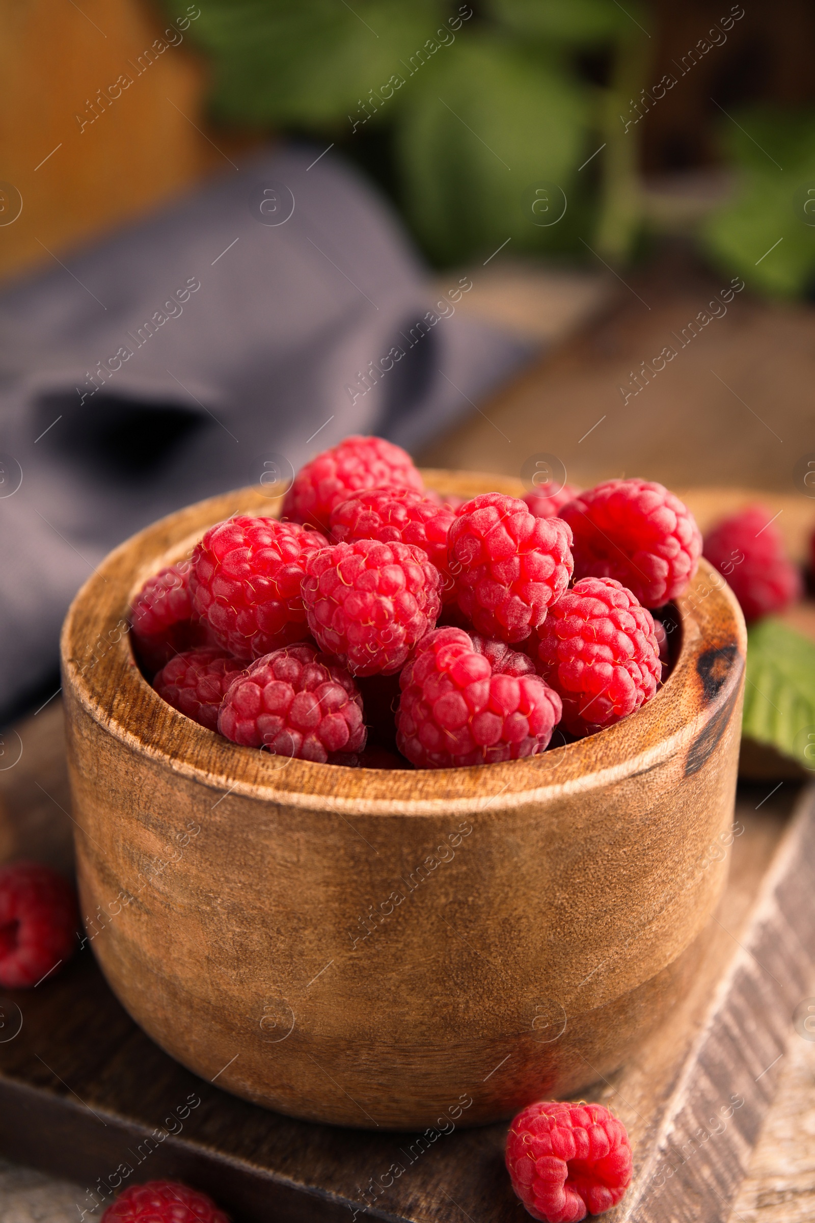 Photo of Bowl of fresh ripe raspberries on wooden board, closeup