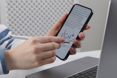 Image of Electronic signature. Woman using stylus and mobile phone at table, closeup