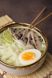 Photo of Bowl of delicious rice noodle soup with meat and egg on brown table, closeup