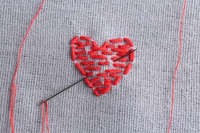 Photo of Embroidered red heart and needle on gray cloth, top view