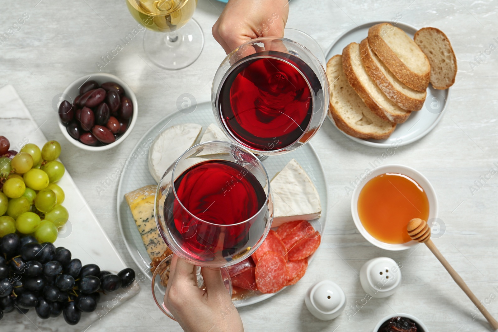 Photo of People holding glasses of red wine over table with snacks, above view
