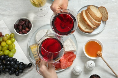 People holding glasses of red wine over table with snacks, above view