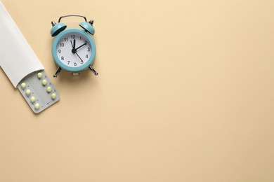 Photo of Oral contraceptive pills and alarm clock on beige background, flat lay. Space for text