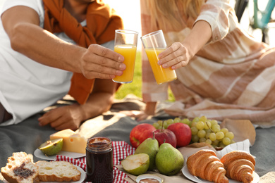 Photo of Young couple having picnic outdoors, focus on hands with glasses of juice