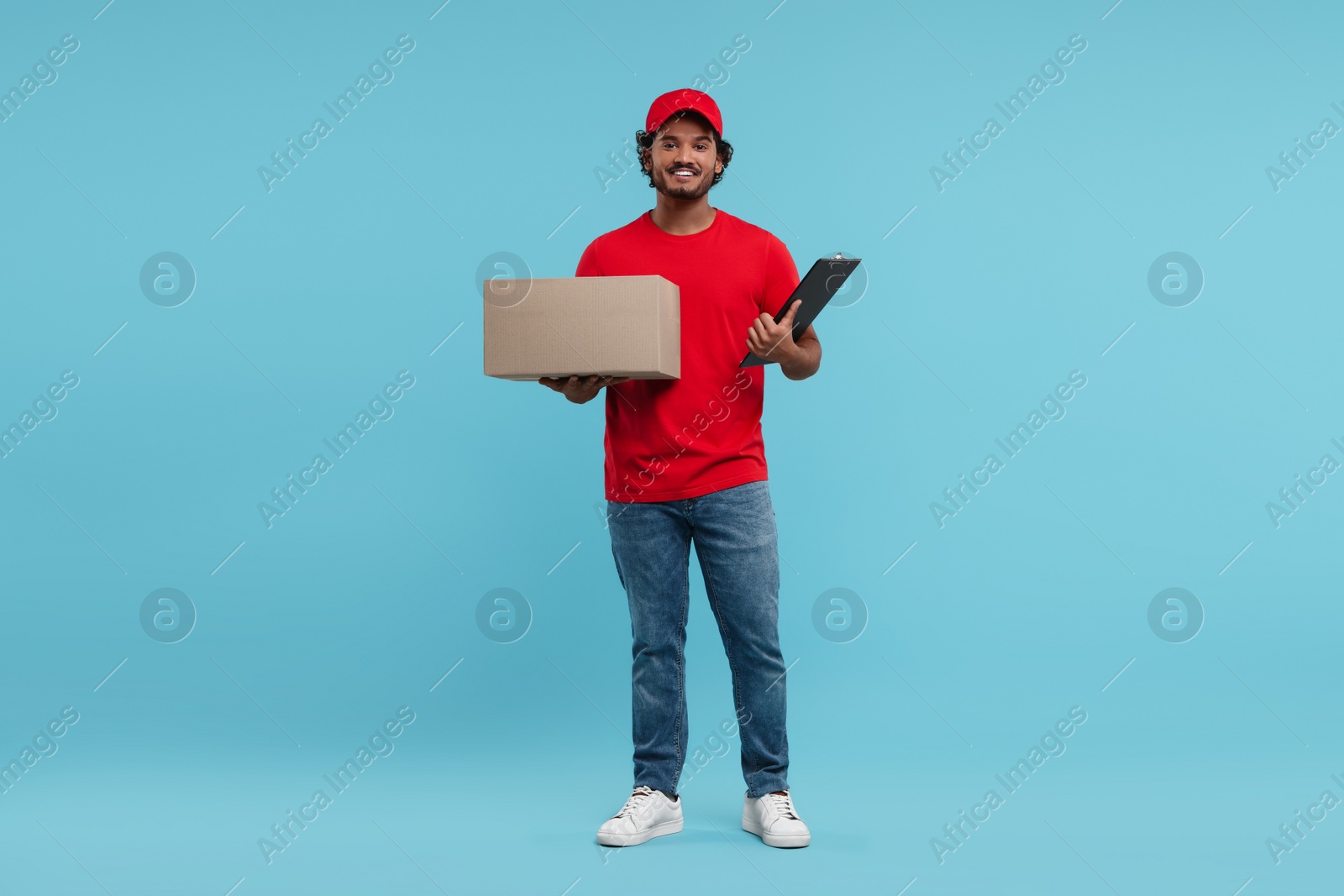 Photo of Happy young courier with parcel and clipboard on light blue background