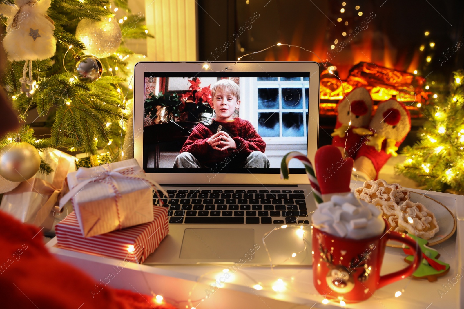 Photo of MYKOLAIV, UKRAINE - DECEMBER 23, 2020: Woman with sweet drink watching Home Alone movie on laptop at home, closeup. Cozy winter holidays atmosphere