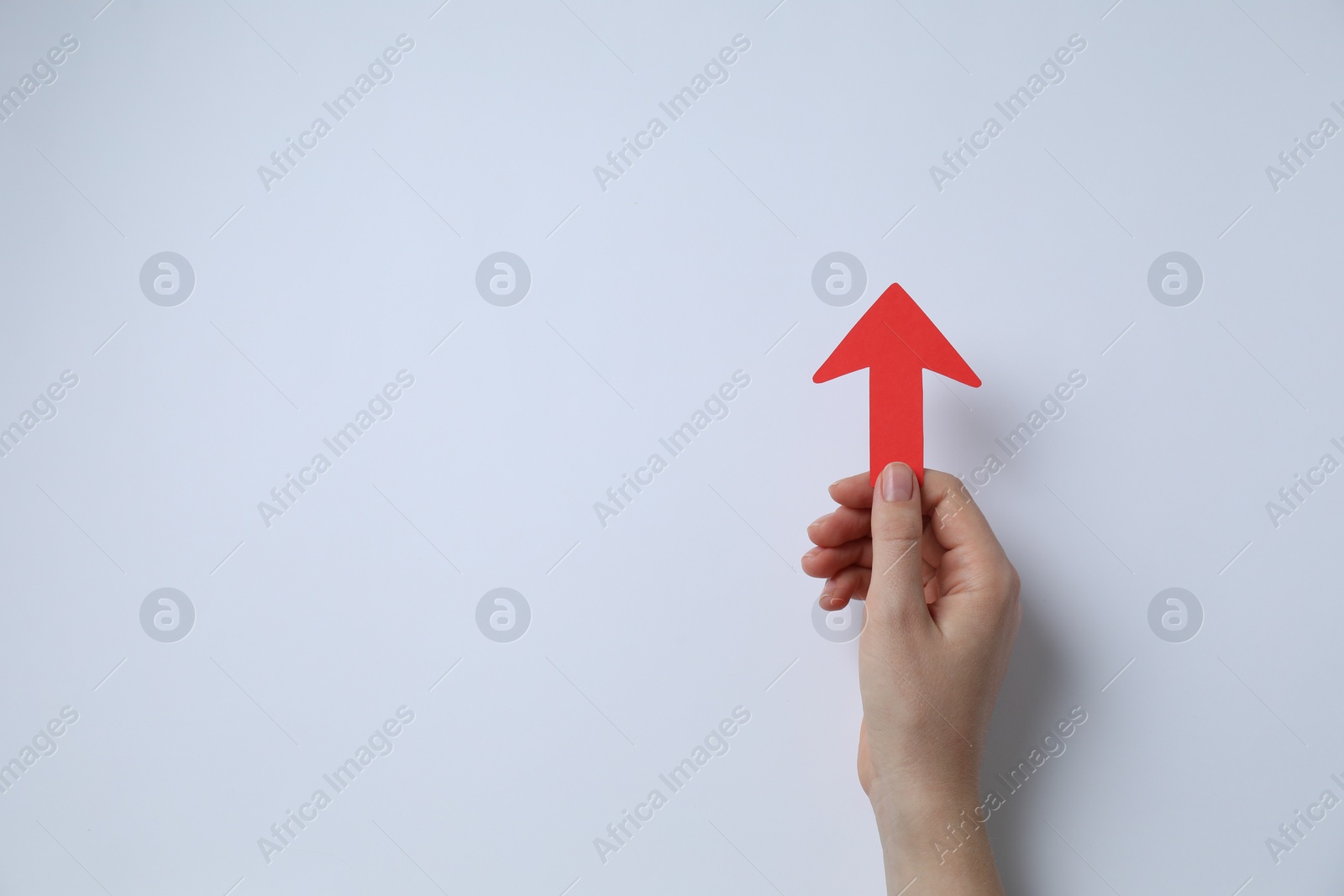 Photo of Woman holding red paper arrow on white background, top view. Space for text