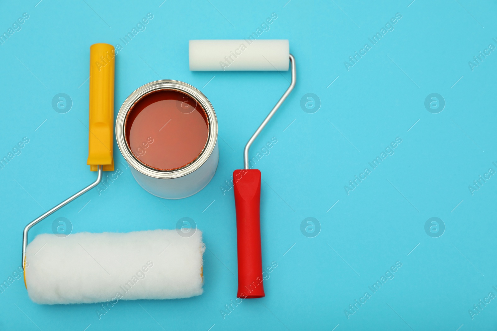 Photo of Can of orange paint and rollers on turquoise background, flat lay. Space for text