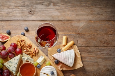 Composition with board of delicious cheese and snacks on wooden background, top view. Space for text