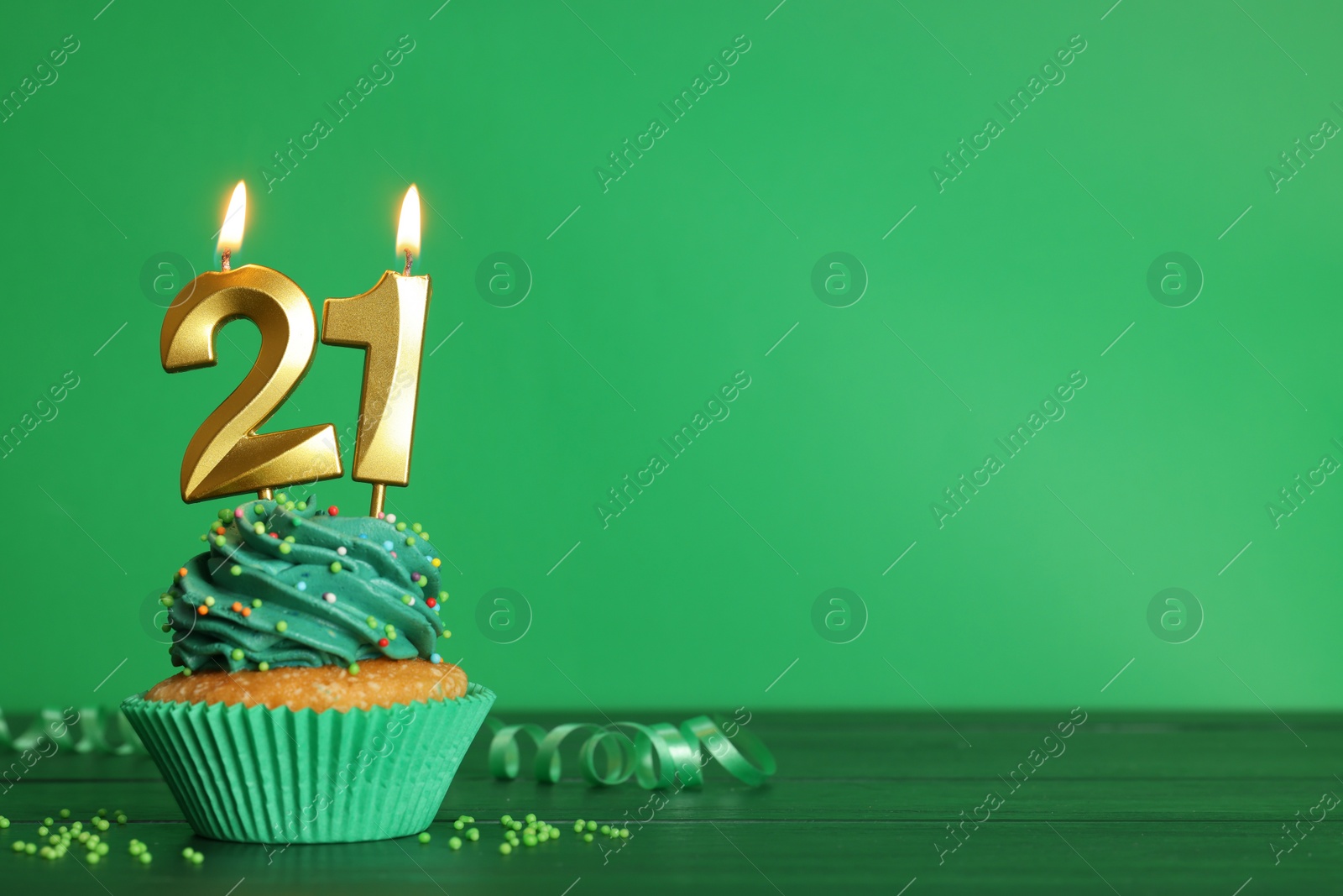 Photo of Coming of age party - 21th birthday. Delicious cupcake with number shaped candles on green wooden table, space for text