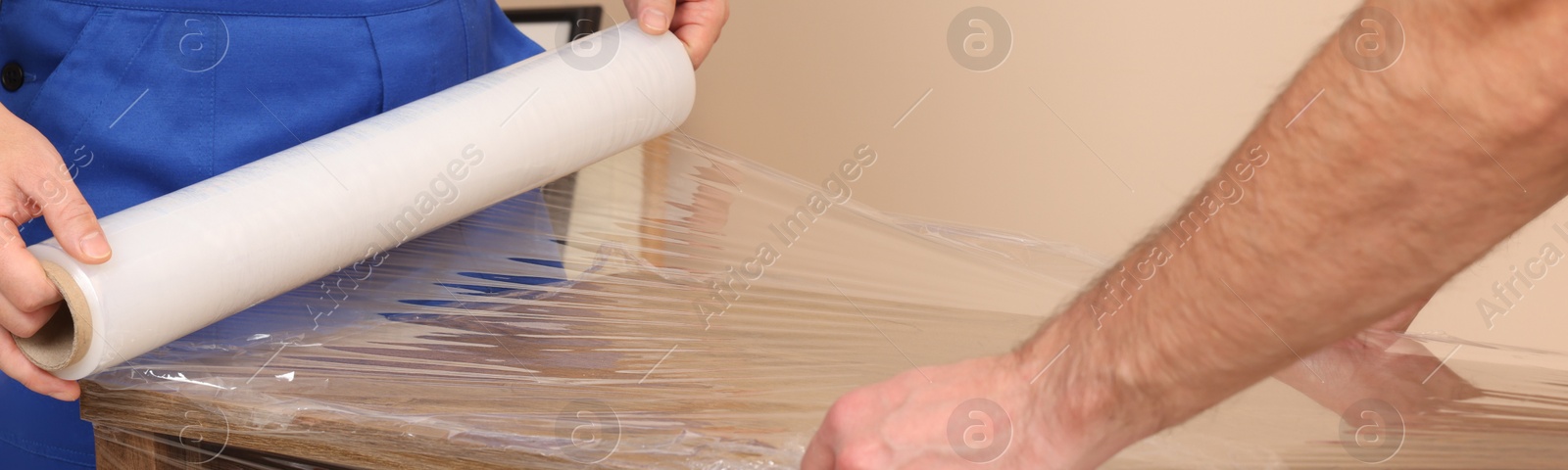 Image of Workers wrapping chest of drawers in stretch film indoors, closeup. Banner design