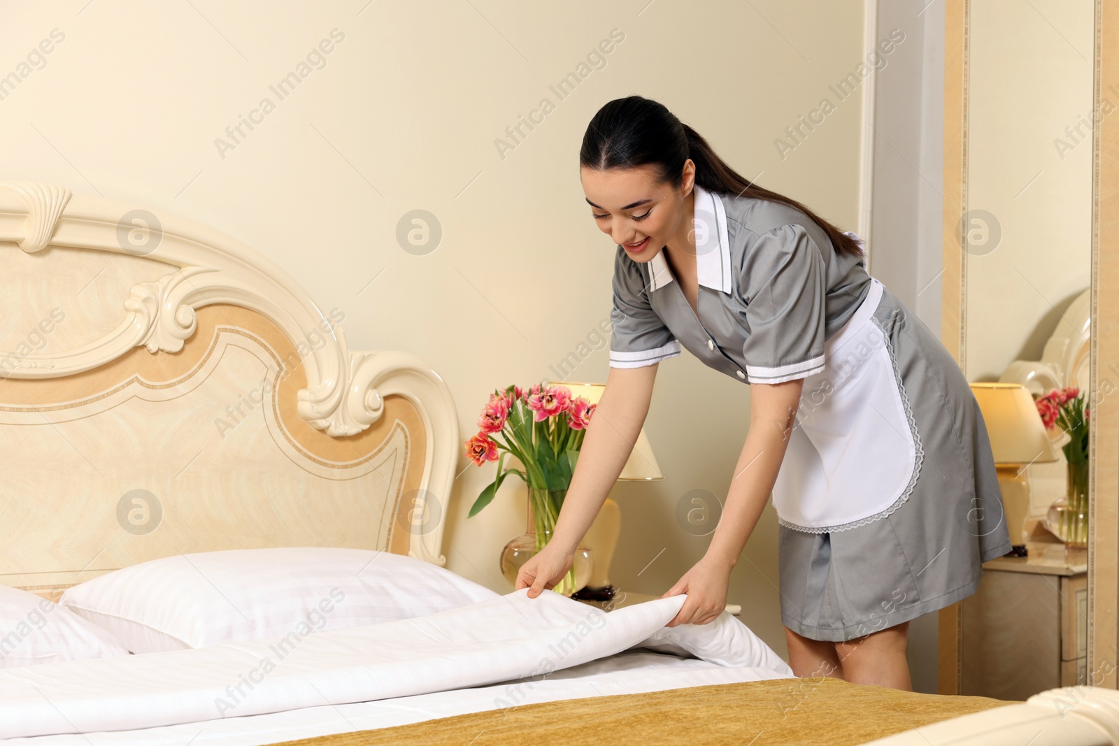 Photo of Young chambermaid making bed in hotel room. Space for text