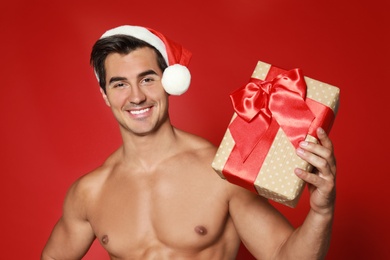 Photo of Sexy shirtless Santa Claus with gift on red background