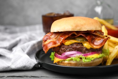 Tasty burger with bacon, vegetables and patty served with french fries on grey wooden table, closeup. Space for text