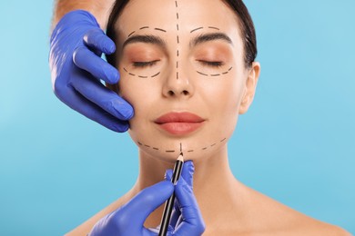 Photo of Doctor drawing marks on woman's face for cosmetic surgery operation against light blue background