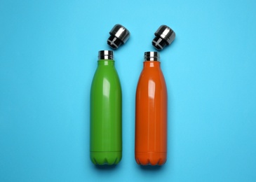 Modern thermo bottles on light blue background, flat lay