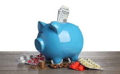 Photo of Piggy bank with money and pills on wooden table against white background. Medical insurance