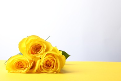 Photo of Beautiful fresh roses on yellow table against white background. Space for text