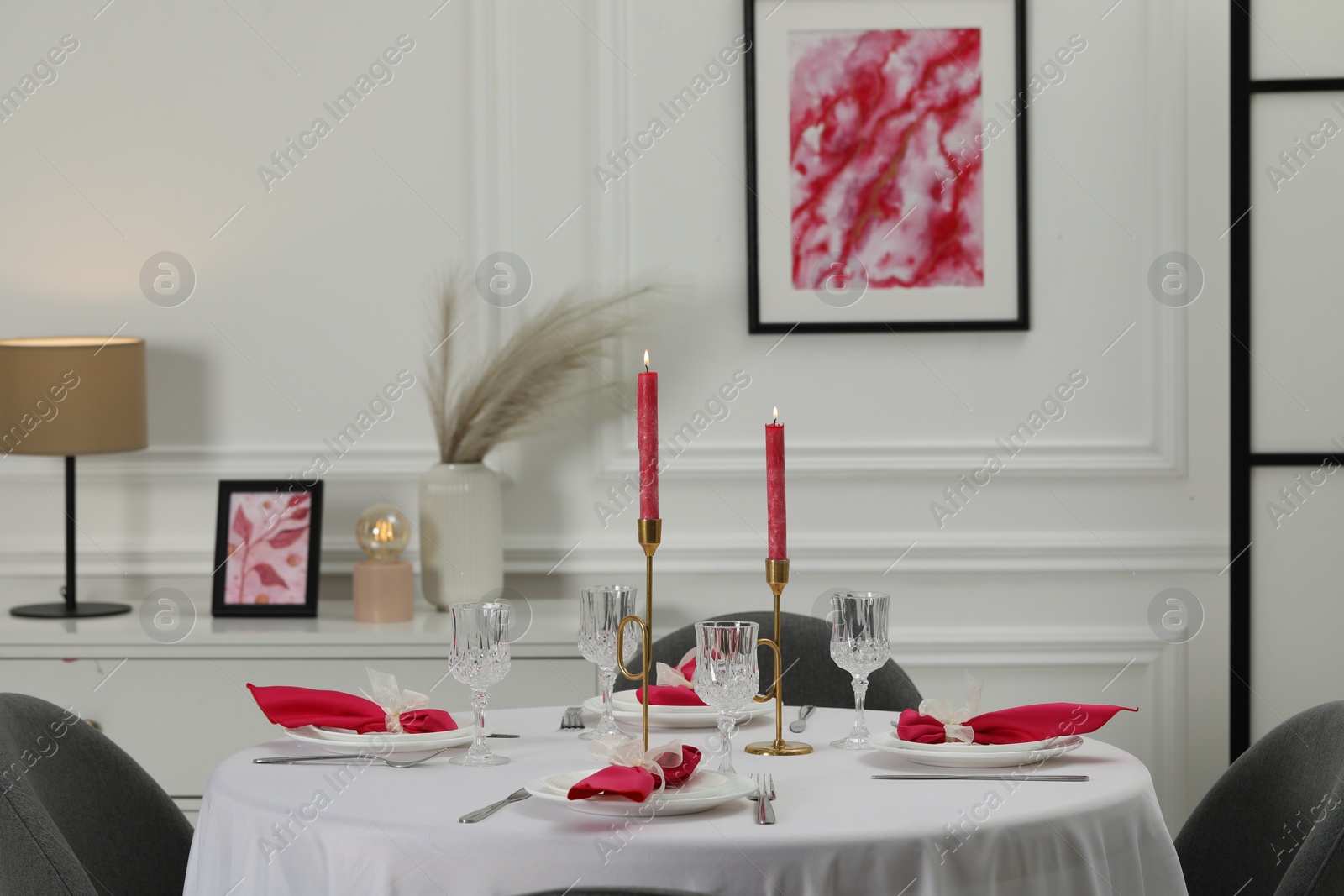 Photo of Color accent table setting. Glasses, plates, burning candles and pink napkins on table in dining room