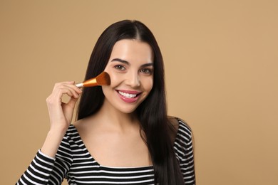 Beautiful woman applying makeup on light brown background. Space for text