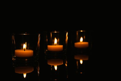 Burning candles in glass holders on table against dark background