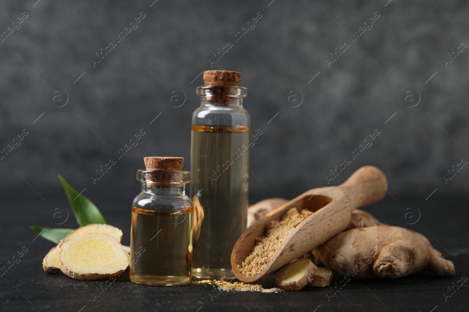 Photo of Glass bottles of essential oil, ginger powder and root on dark table